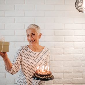 Mature woman holding a birthday cake and a gift