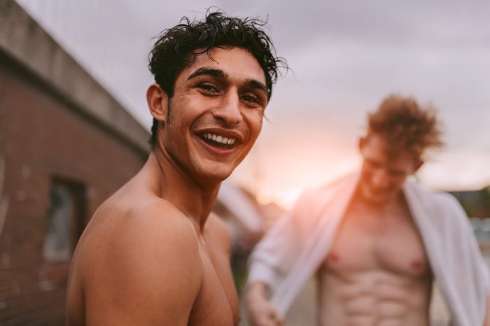 Portrait of handsome young man shirtless looking at camera and smiling with friends in background.