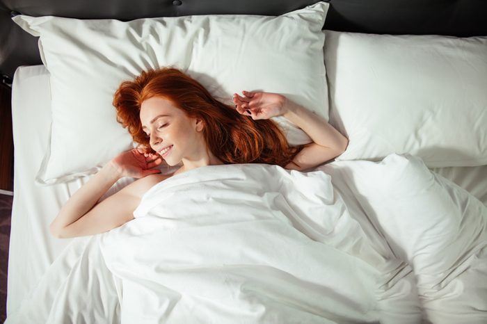 Redhead sleeping young woman lies in bed with eyes closed. top view