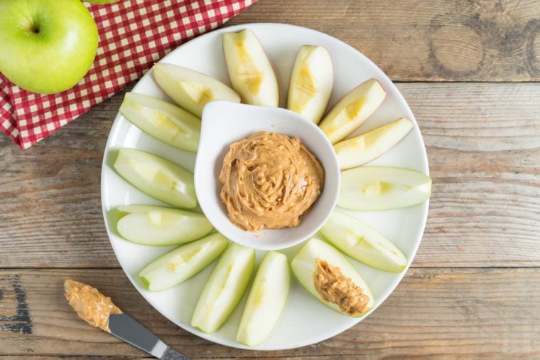 Green apple sliced dip with peanut butter on plate. Diet and Healthy food. Top view.