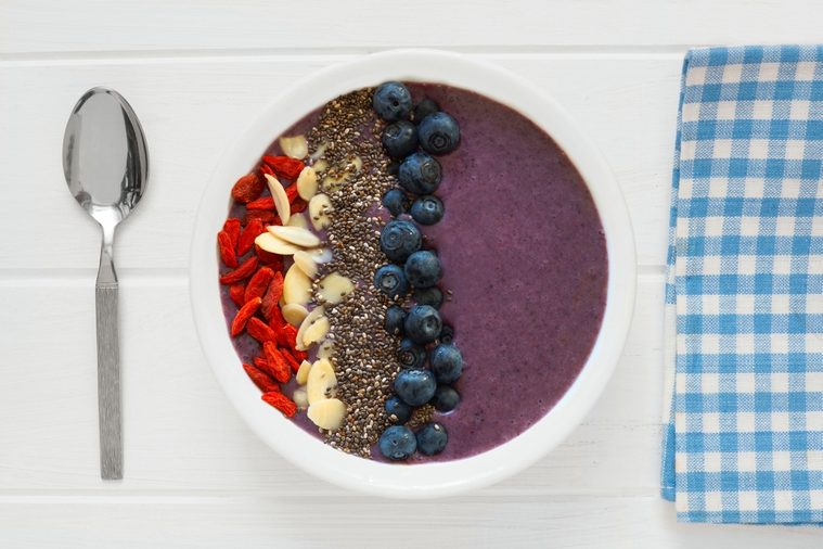 Nutritious blueberry smoothie bowl with goji berries, almonds and chia seeds on white wood with cloth and spoon