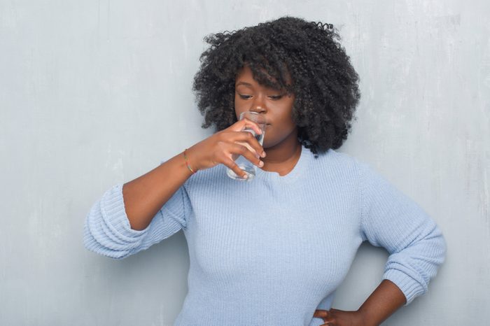 Young african american woman over grey grunge wall drinking a glass of water with a confident expression on smart face thinking serious