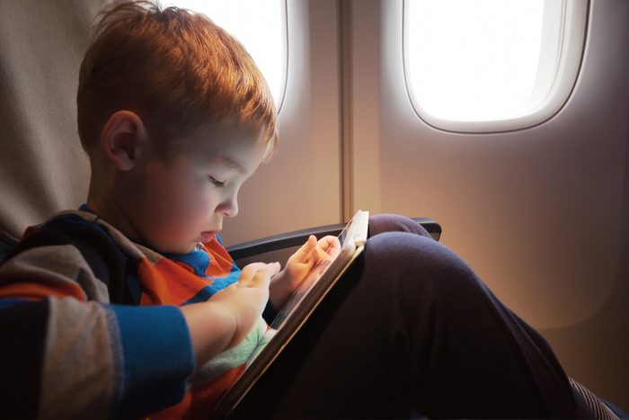 Little child with tablet computer on the lap sitting by the illuminator in the plane