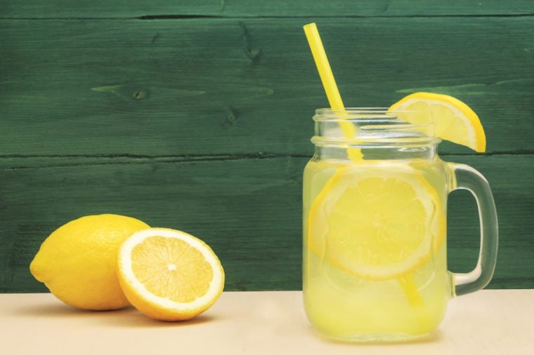 Mason jar glass of lemon lemonade with lemons and straw on table and wooden background. Cold summer beredge. Mojito drink. Lemon water