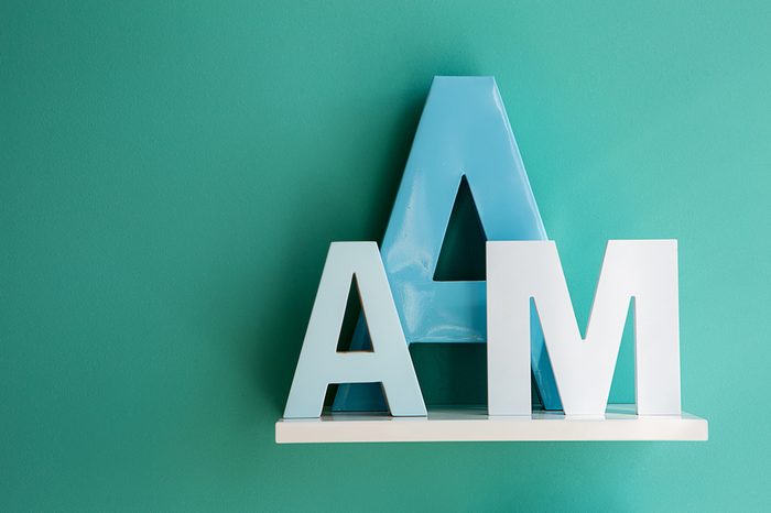 Letters A small and big size turquoise color and letter M on a white shelf. Shelf installed on a wall in a horizontal position. Fragment of interior decor.