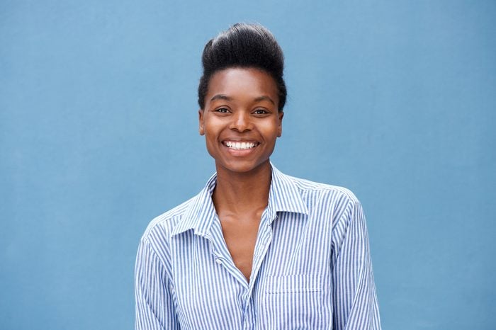 Close up portrait of beautiful young black woman smiling against blue background
