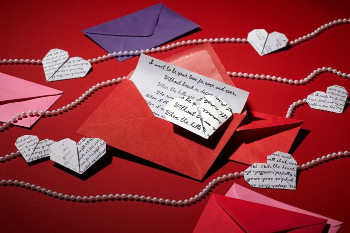 poetry pages folded into the shape of hearts with red, pink, and purple love letter envelopes and strings of pearls on dark red background