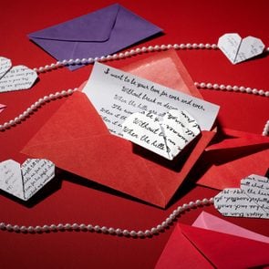 poetry pages folded into the shape of hearts with red, pink, and purple love letter envelopes and strings of pearls on dark red background
