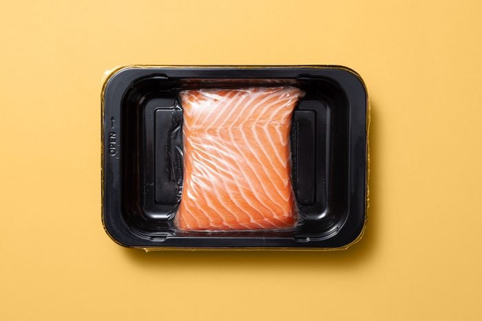 Raw Salmon in a black plastic tray package on a yellow background 