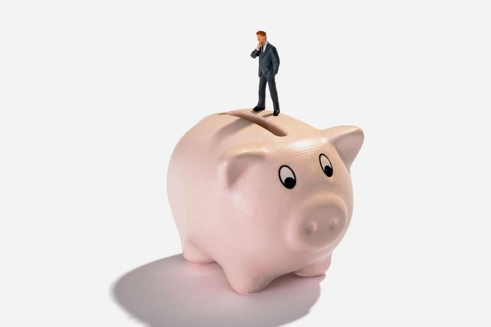 Studio shot close-up of a miniature figure man thinking of savings and profit while standing on a piggy bank against white background for copy space