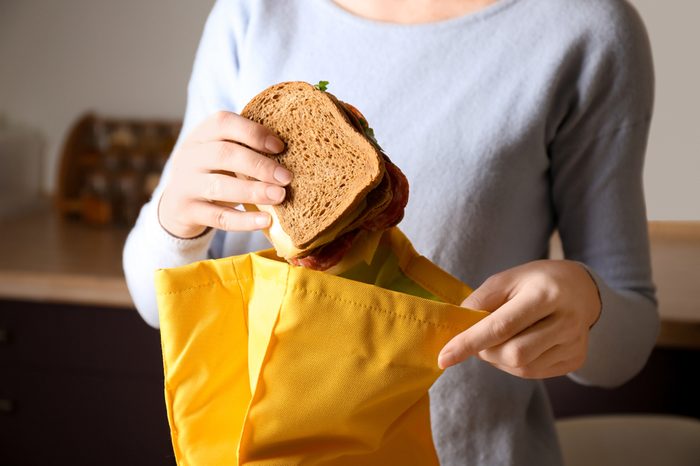 Mother packing food into school lunch bag indoors