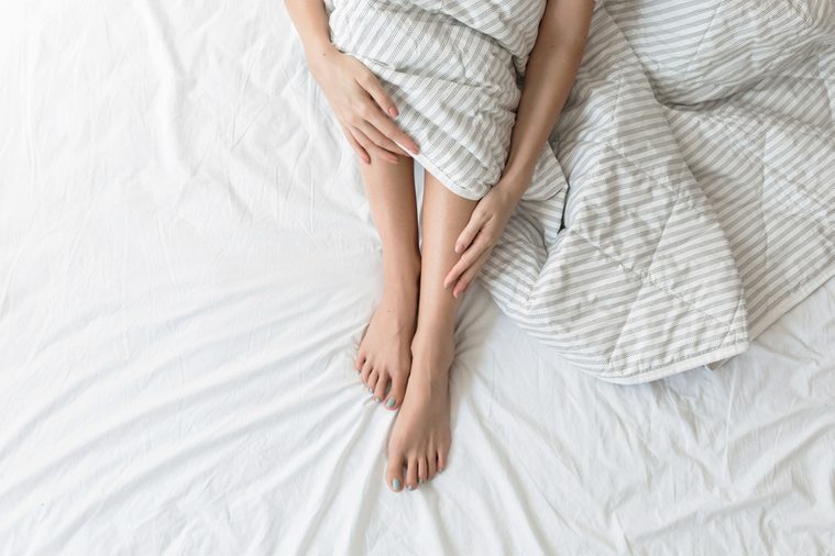 Legs and arms of unrecognisable woman sitting on her bed.