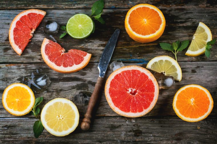 Set of sliced citrus fruits lemon, lime, orange, grapefruit with mint, ice and vintage knife over wooden background. Top view.
