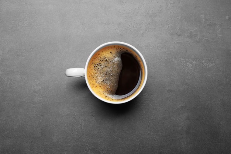 Cup of coffee on grey background, top view