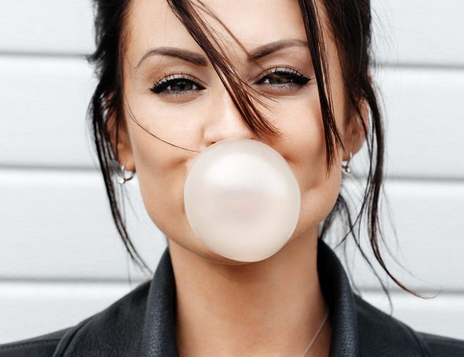 Outdoor lifestyle portrait of beautiful young woman blowing a bubble gum balloon