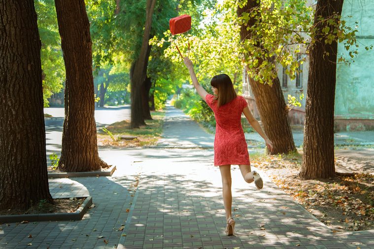 Young beautiful girl having fun skipping walking down the street, waving her handbag