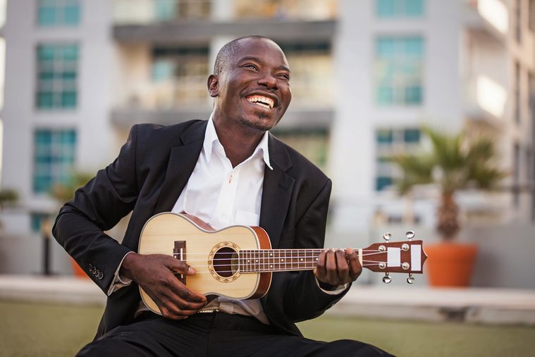 black smiling man wearing formals playing a guitar