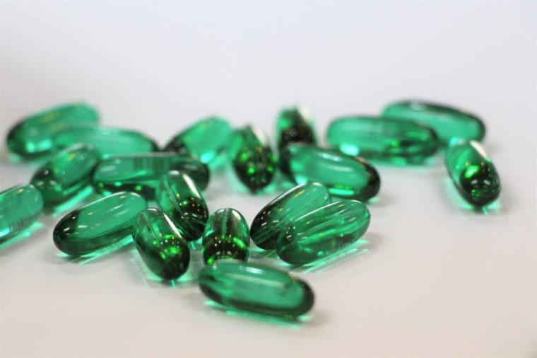 Green gel capsules of pain killer on white background.
