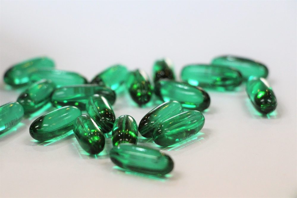 Green gel capsules of pain killer on white background.