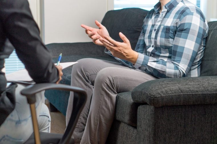 Man talking and waving hands in therapy session with psychiatrist, psychologist, counselor, therapist or life coach. Meeting with professional specialist with a notepad. Male patient sitting on couch.