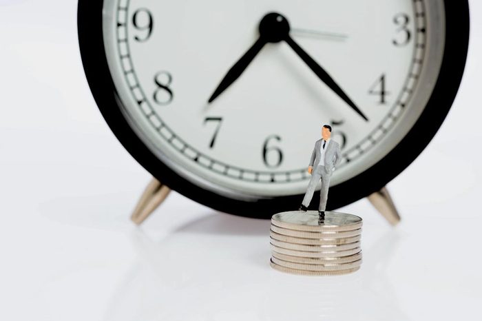 Miniature business people stand on silver coins with alarm clock background,time is money concept