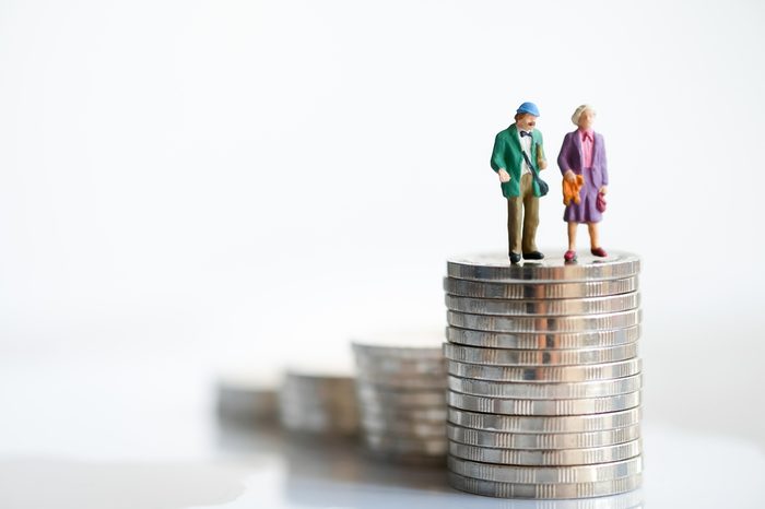 Miniature people: Old couple figure standing on top of stack coins using as background retirement planning concept.