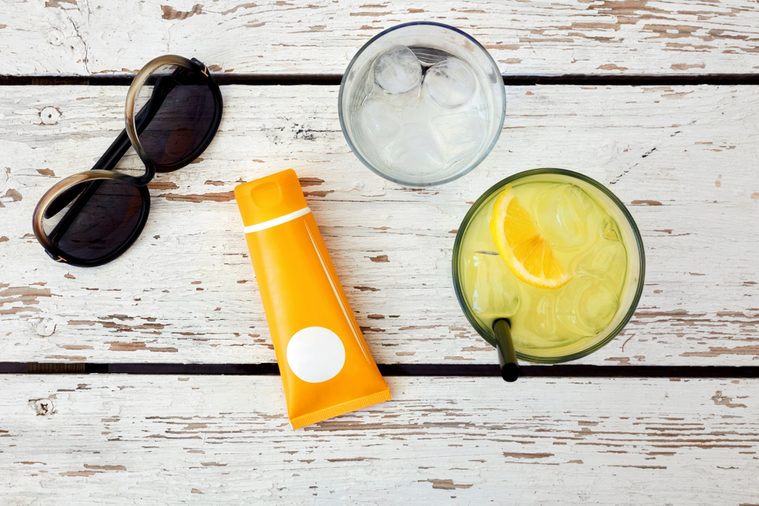 Top view of sunglasses, sunblock, glass of lemonade and water on a white wooden table. Concept of beach accessories and holiday