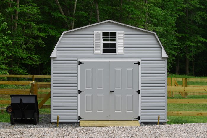 A nice new storage shed outside of a fenced in back yard with a trailer beside it with room for your text.