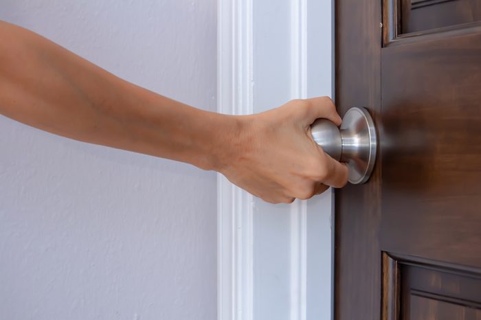 a woman's right hand turning a doorknob to close or open it palm turned away from camera, privacy trust safety security concept, horizontal shot, white copy text space, closeup side view