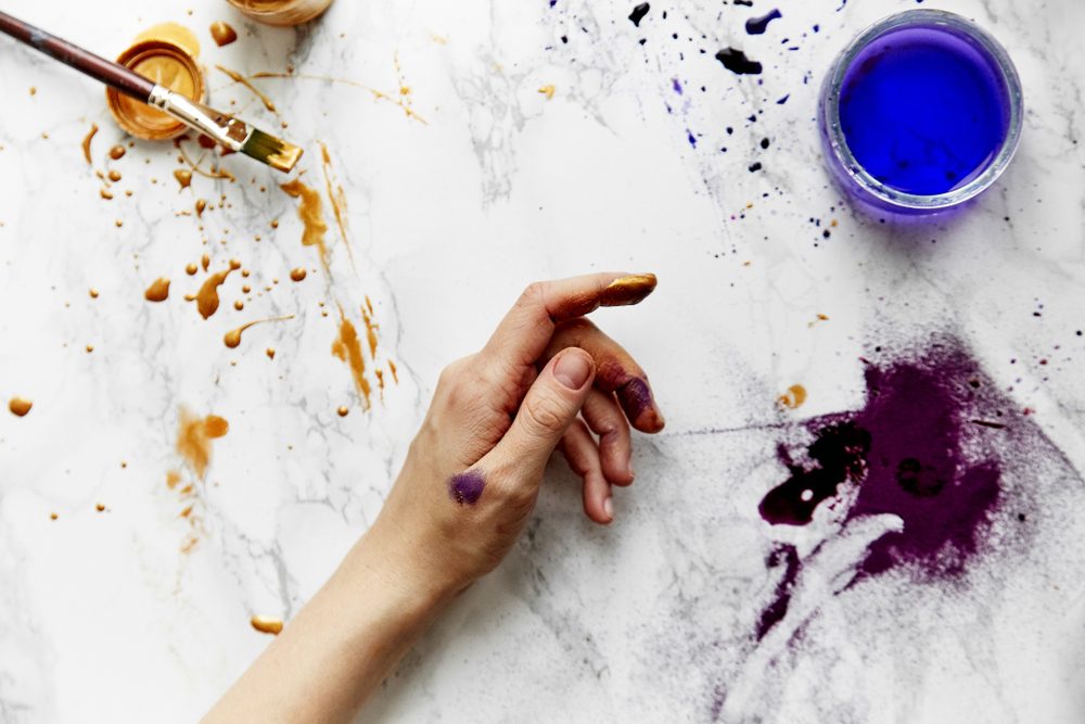 Overhead view of female artist hands soiled with golden and violet paints on white background. Artist workspace concept.