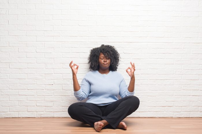 Young african american woman sitting on the floor at home relax and smiling with eyes closed doing meditation gesture with fingers. Yoga concept.