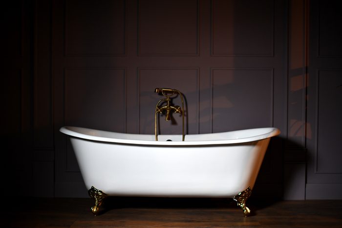 Beautiful classic style white claw foot bathtub with stainless steel old fashioned faucet and sprayer on dark background