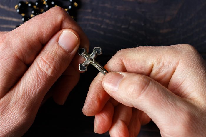 The hand holds a rosary close-up on a dark wooden background