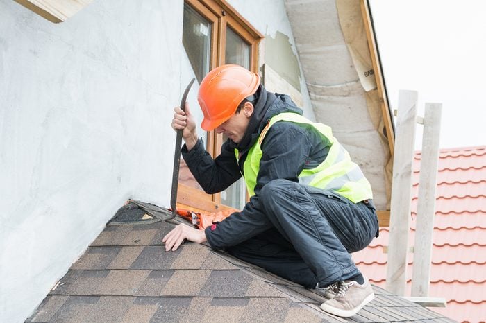 Roofer builder worker dismantling roof shingles