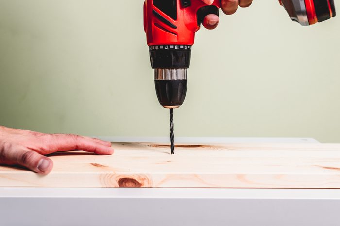 A red screwdriver drills a hole in a wooden board. Making wooden products, the concept of manual labor.