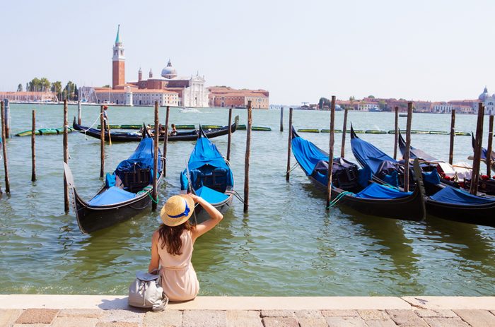 Beautiful sunny Venice-girl sitting on the pier, near the gondola.