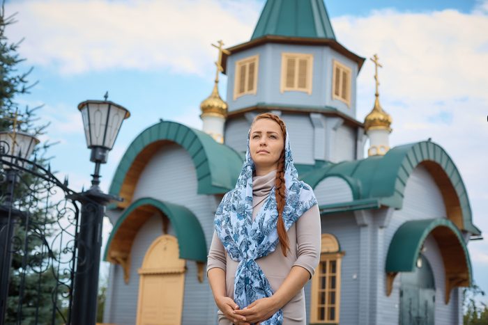 Russian Orthodox middle-aged woman in a scarf stands on the background of the Orthodox wooden Church.