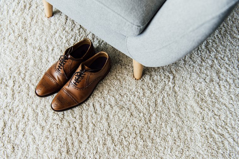 close up of leather oxford shoes on carpet near textile armchair