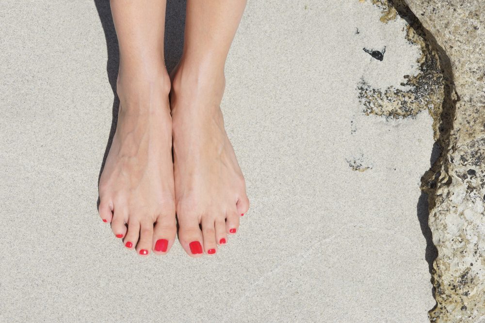 Pretty woman feet with red pedicure: relaxing on sand. Holiday, vacation, spa, summer: concept.