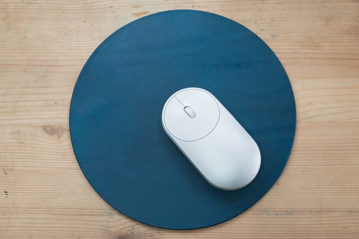 White and silver wireless mouse on a navy blue round leather mouse pad on a wooden surface