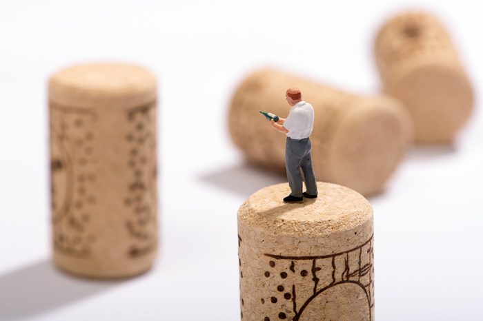 Miniature figure of a sommelier or wine expert standing on a cork looking at a bottle in his hand for pairings at a restaurant