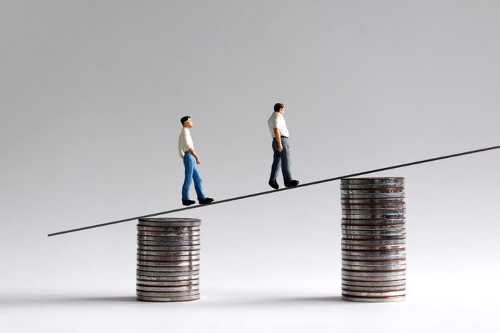 Two miniature men walking on two piles of coins.