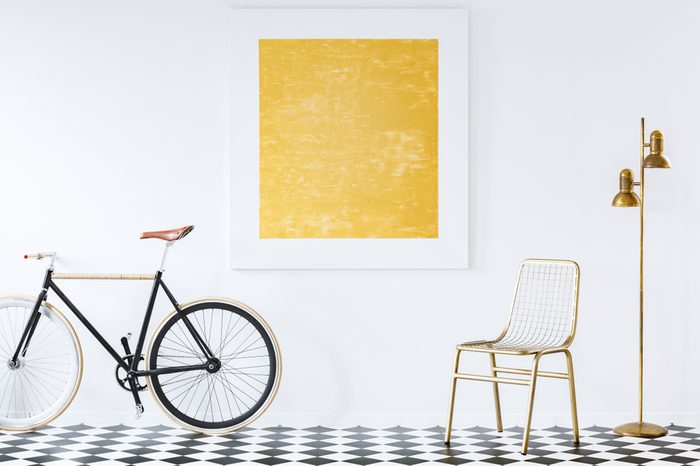 Old-fashioned bike in a minimalist, hipster living room interior with golden decor and an abstract oil painting on a white wall