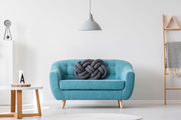 Knot pillow on turquoise sofa in living room interior with gray lamp, ladder and wooden table