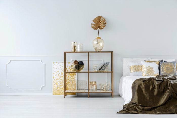 Gold leaf in vase on a shelf against white molding wall in sophisticated bedroom interior with bed