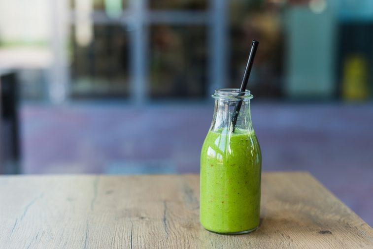 Delicious carrot green spinach, mango and banana cocktail in bottle with straw on wooden table