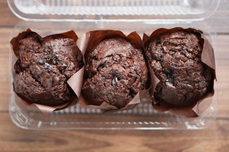 Three delicious chocolate muffins packed in plastic food container. Take away bakery, dessert for coffee. Overhead shot, close up. Fresh brownie cake