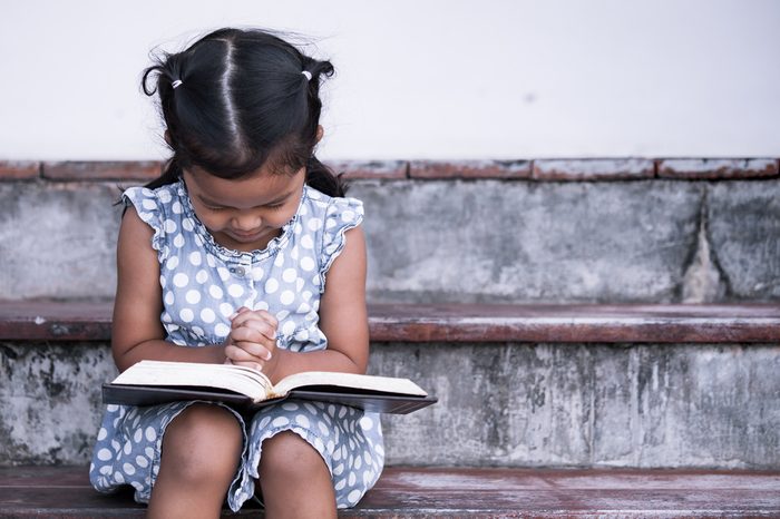Cute asian little girl closed her eyes and folded her hand in prayer on a Holy Bible for faith concept in vintage color tone
