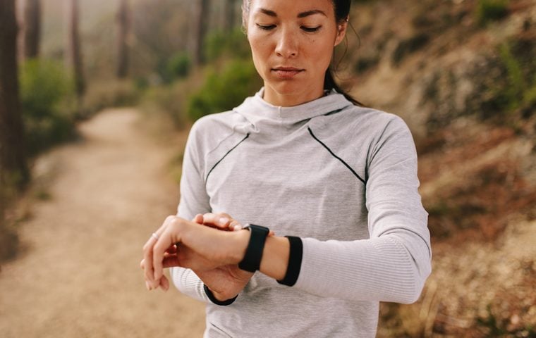 Asian female checking fitness progress on her smart watch. Fit young woman runner checking time on smart watch.