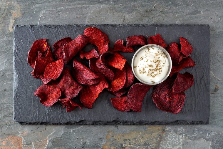 Healthy beet chips with dip, above view on a stone server and slate background